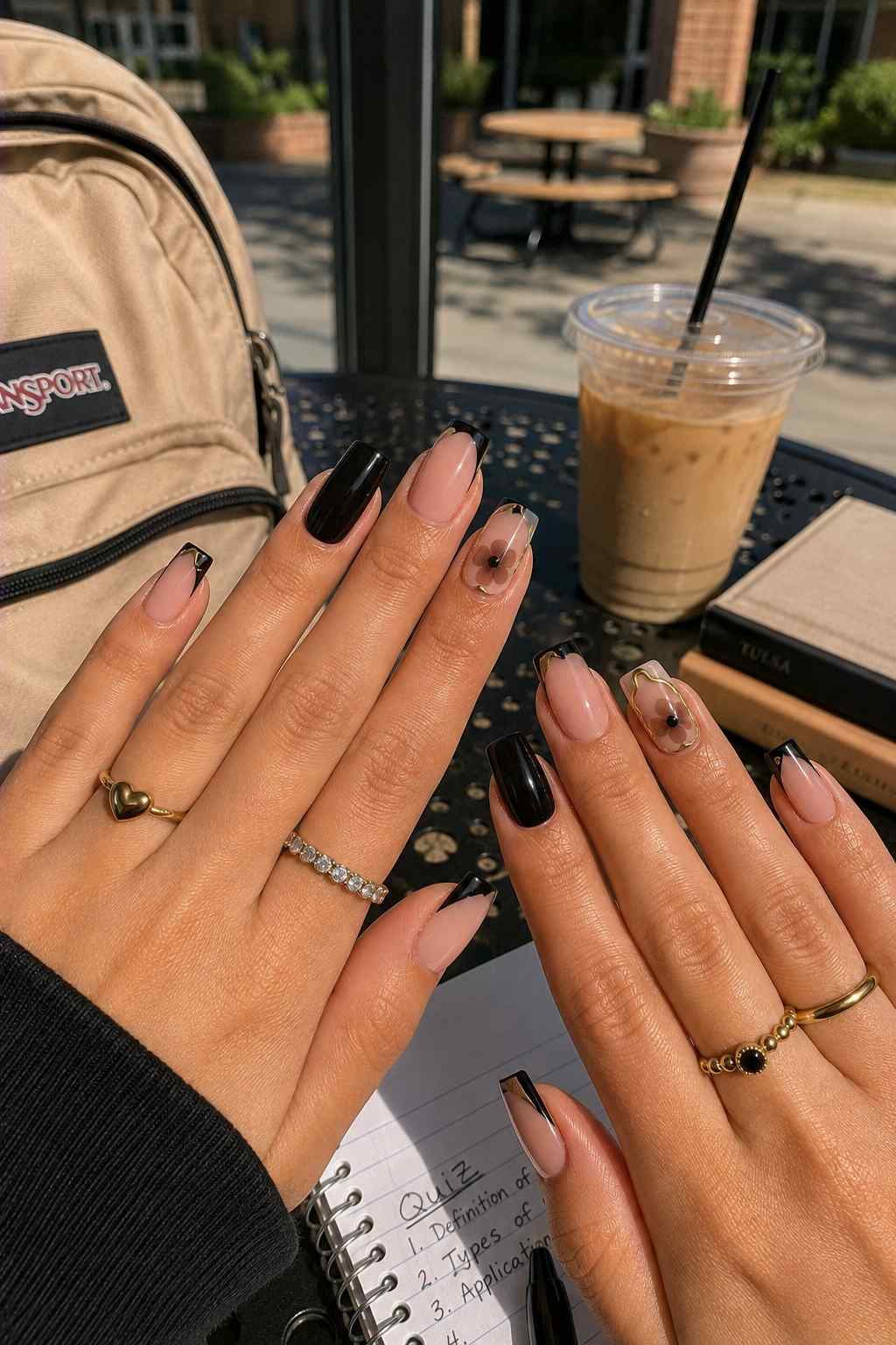 Nude and solid black nails with gold-outlined French tips and a black flower accent nail
