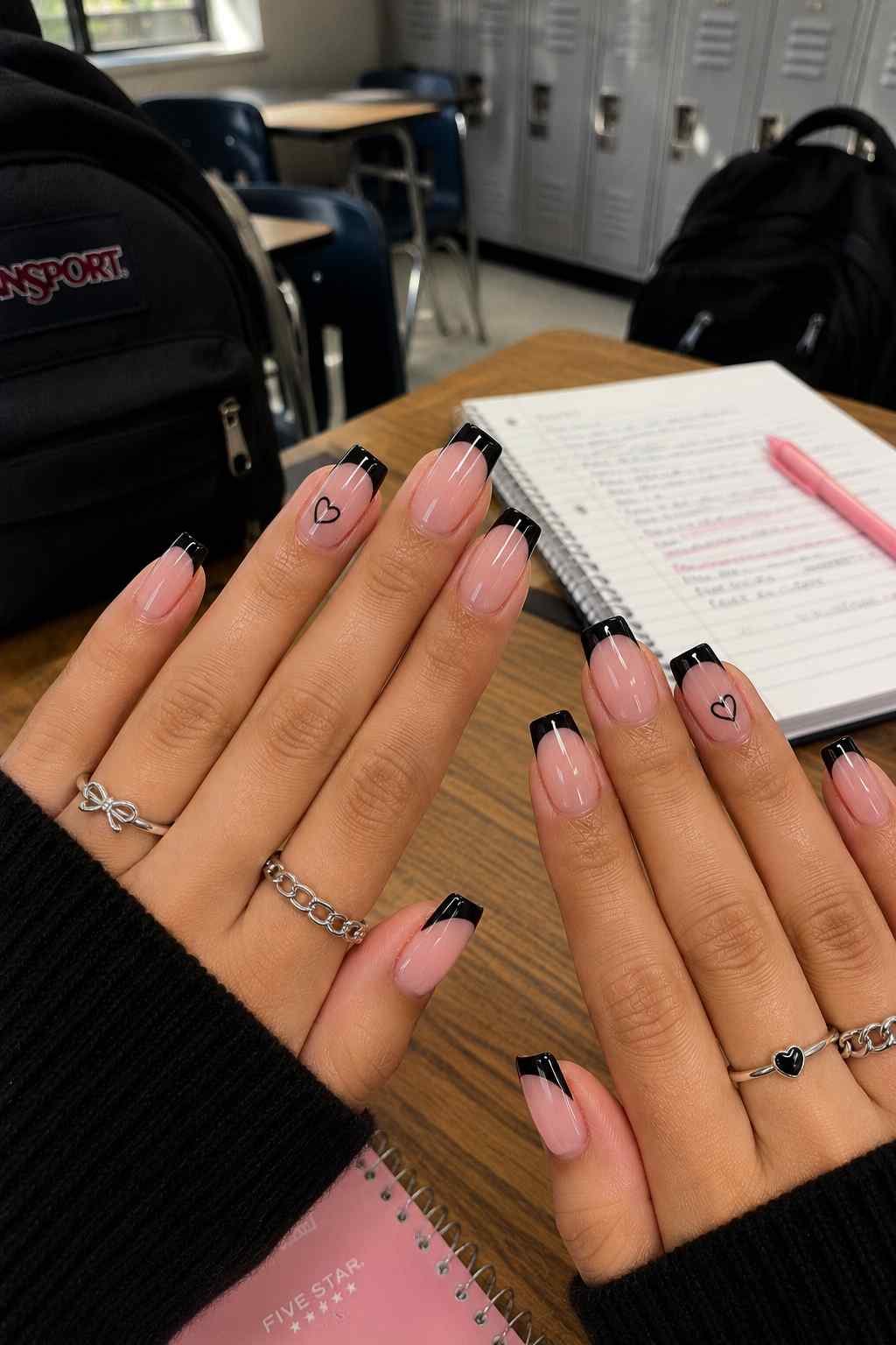 Nude nails with glossy black French tips and hand-painted heart accent nails