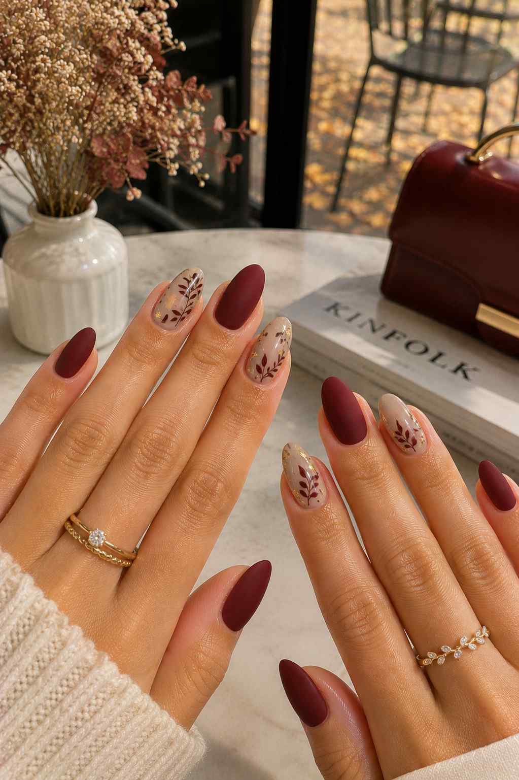 Matte wine red nails paired with sheer nude nails featuring full burgundy botanical leaf art and gold foil