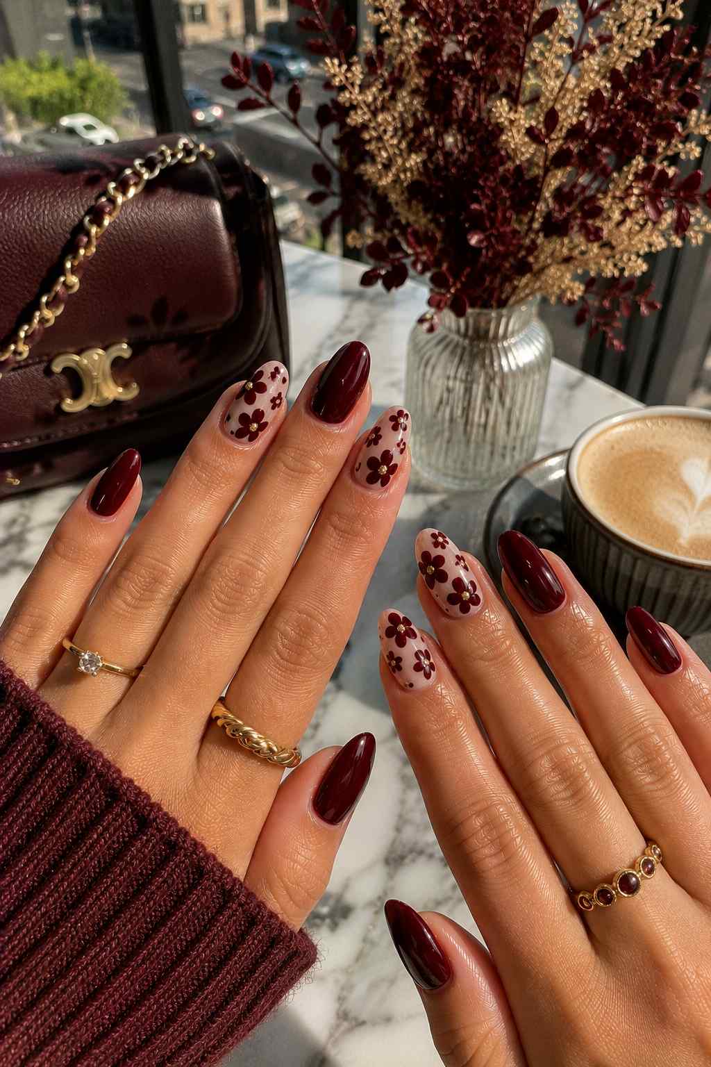 Glossy oxblood nails paired with sheer nude nails featuring hand-painted burgundy flowers with gold centers