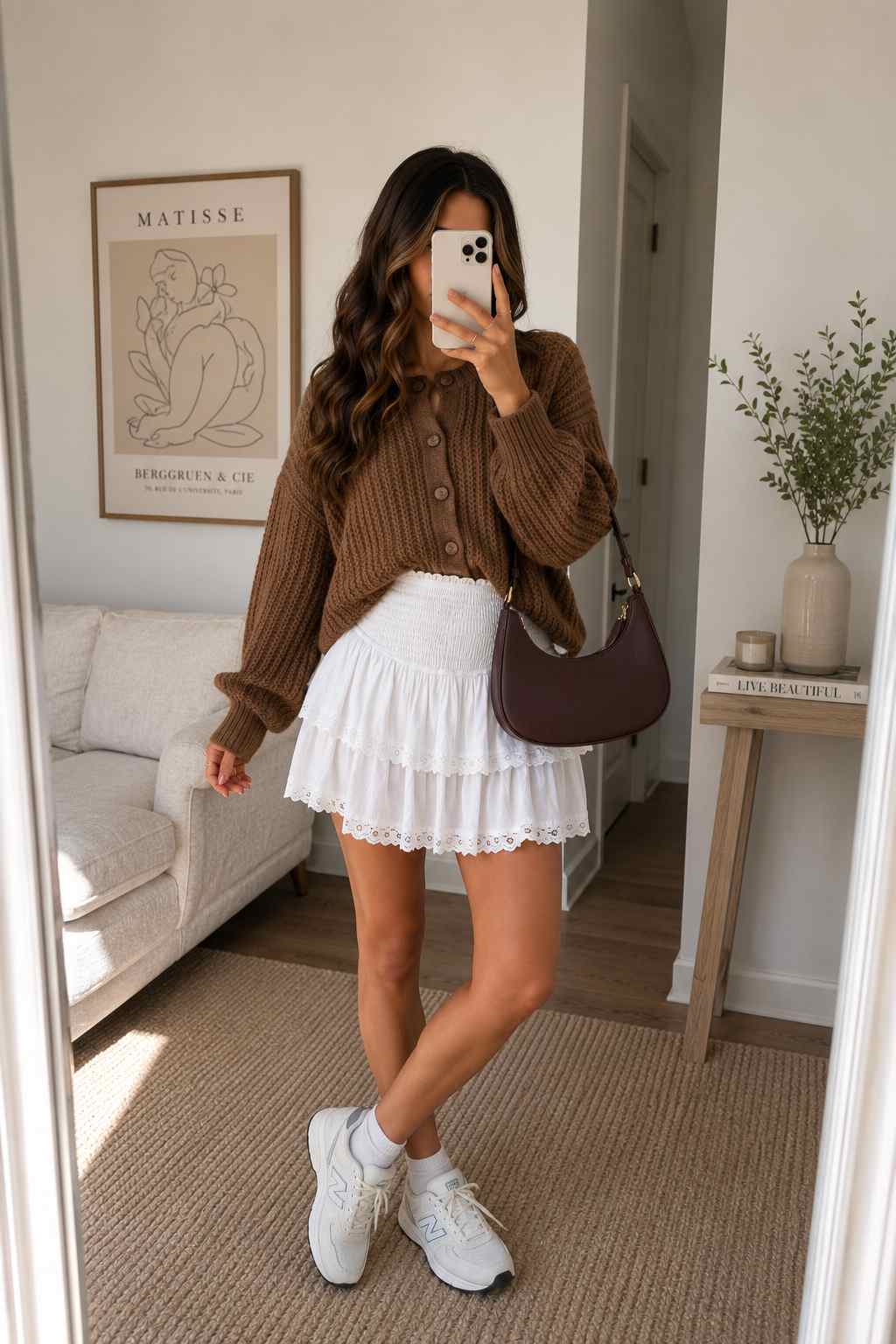 Woman wearing a chunky brown knit cardigan, white tiered eyelet mini skirt, and white sneakers.