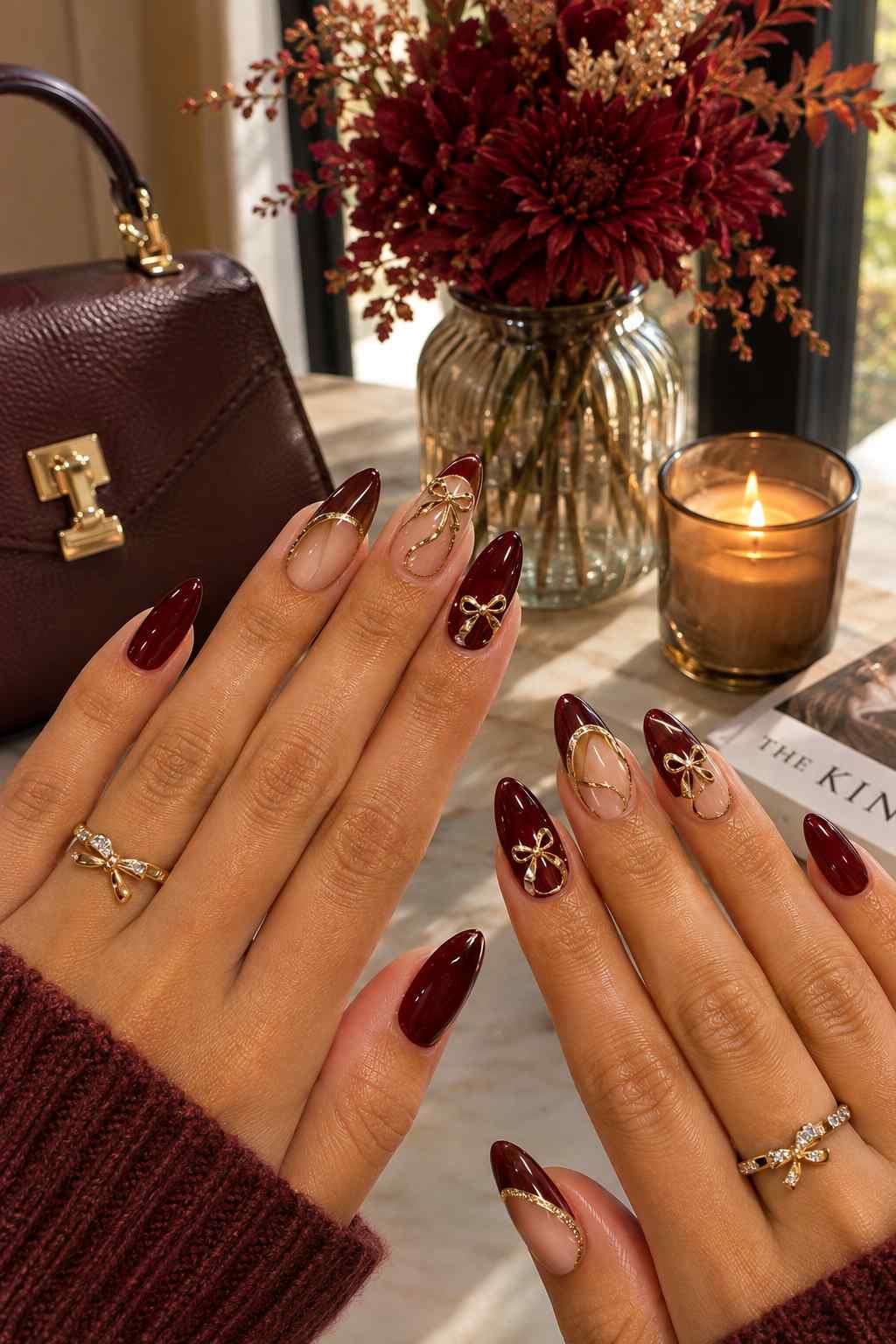 Glossy oxblood nails alternating with sheer nude nails featuring 3D gold bow charms and gold line art