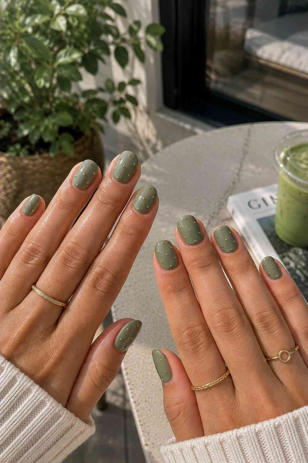Short round sage green nails with a scattering of tiny gold studs