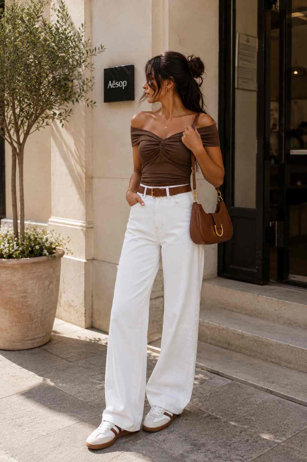Woman wearing a brown twist-front off-the-shoulder top with white wide-leg jeans.