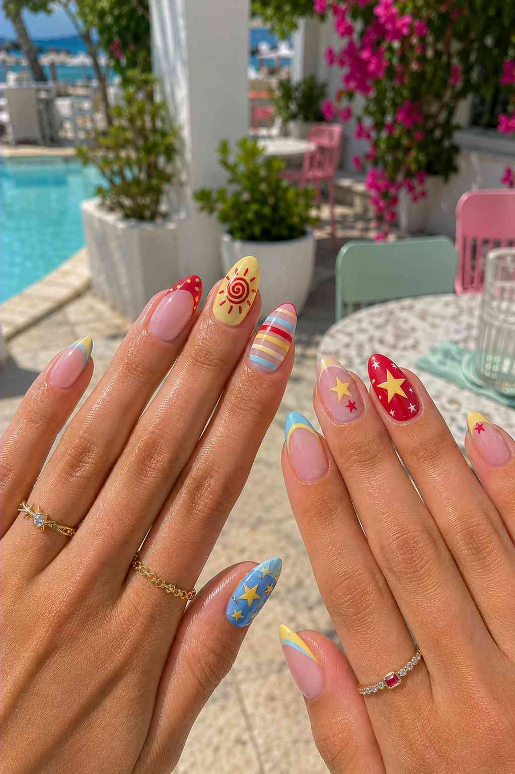 Colorful summer nail set with red polka dots, a painted sun, striped nails, and star designs in red, gold, and blue