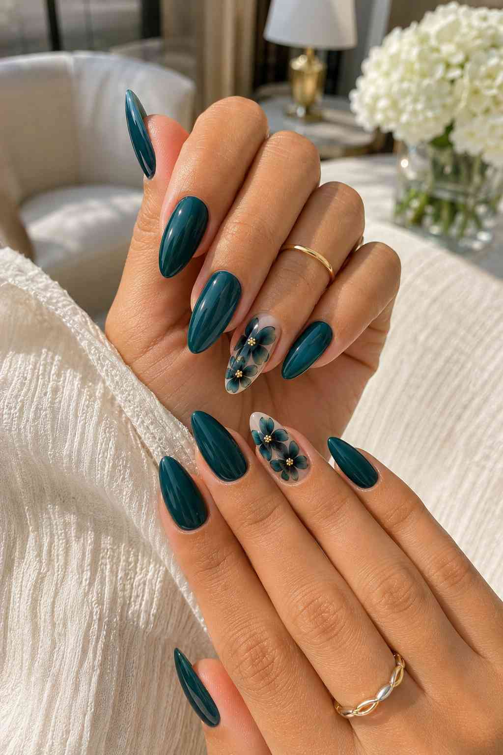 Deep glossy teal almond nails with sheer accent nails featuring dark teal flowers and gold centers