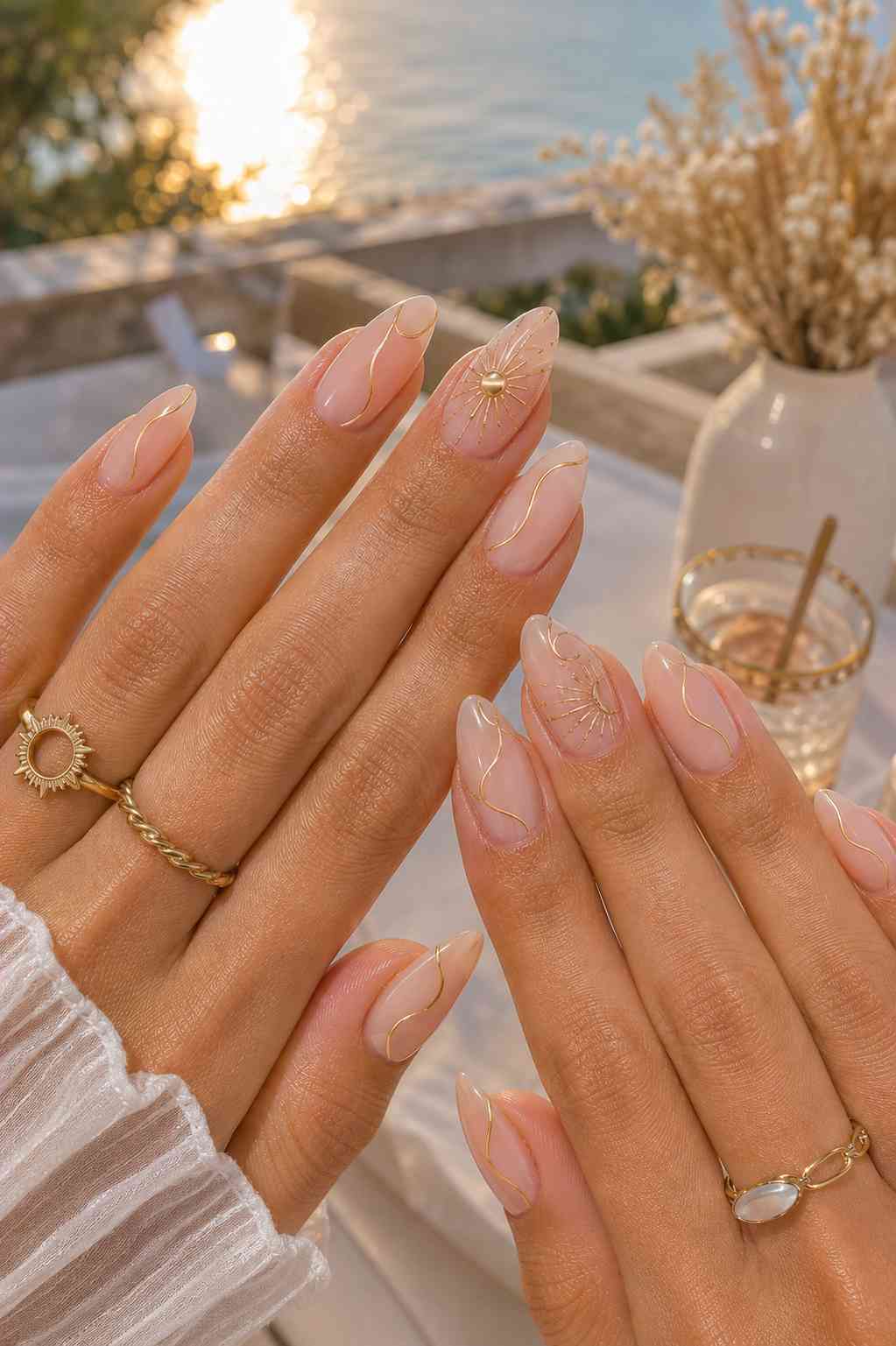 Nude nails with thin gold swirl line art and small gold sunburst charm accents
