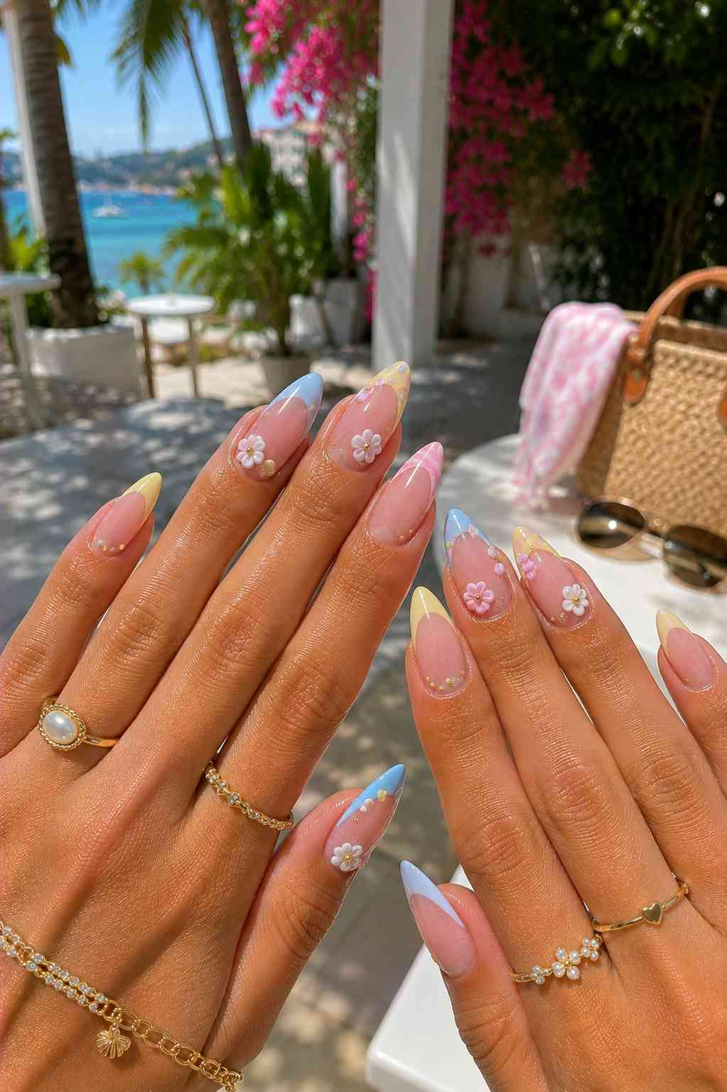 Blue, yellow, and pink French tip nails each finished with a small 3D daisy and gold dots