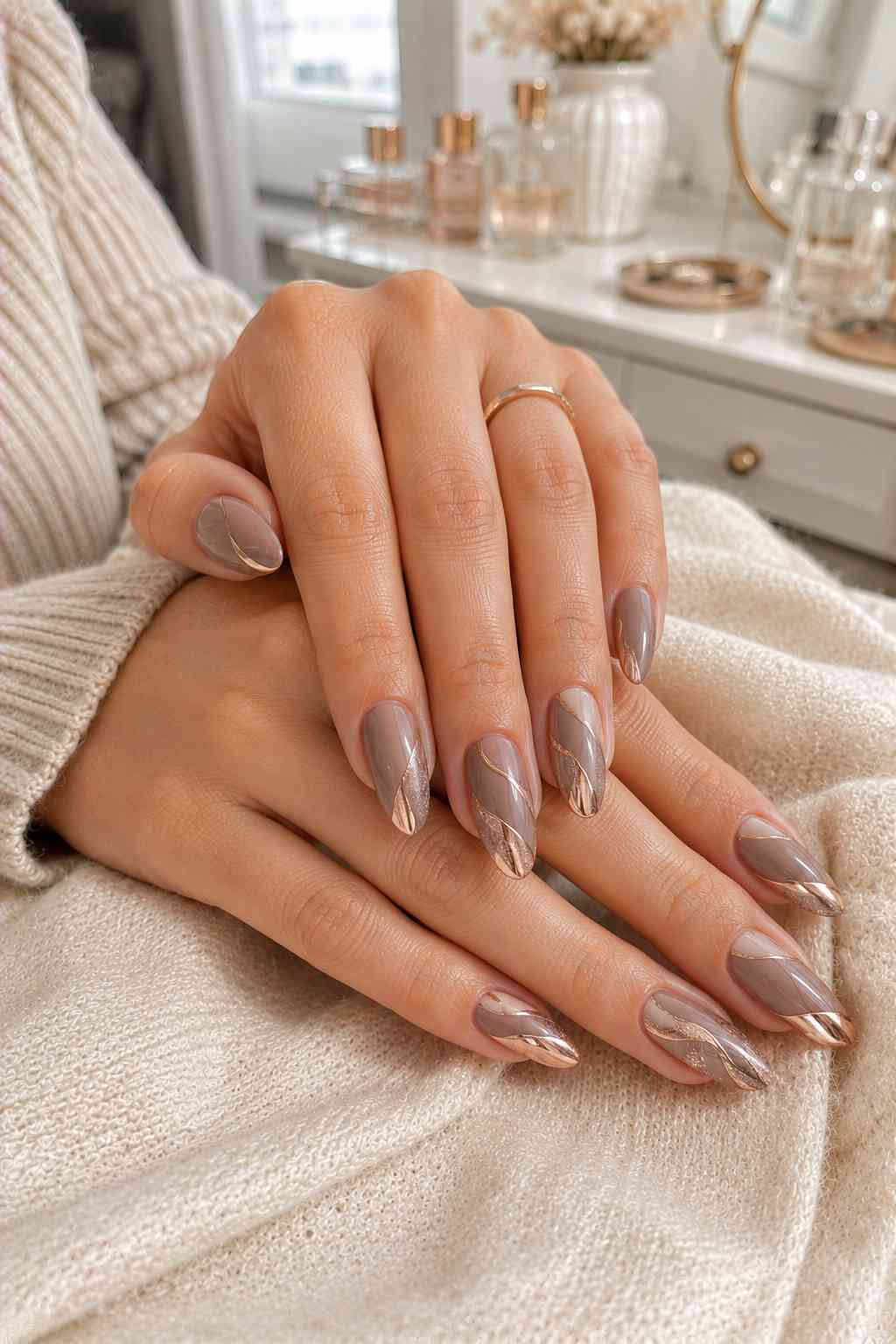 Taupe nails wrapped in a bold rose gold swirl chrome design