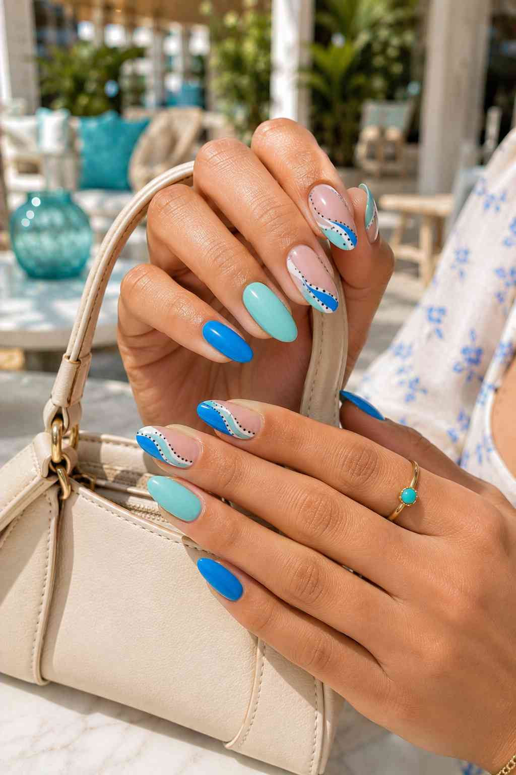 Teal and bright blue almond nails with sheer accent nails featuring blue, aqua, and white wavy designs with black dots