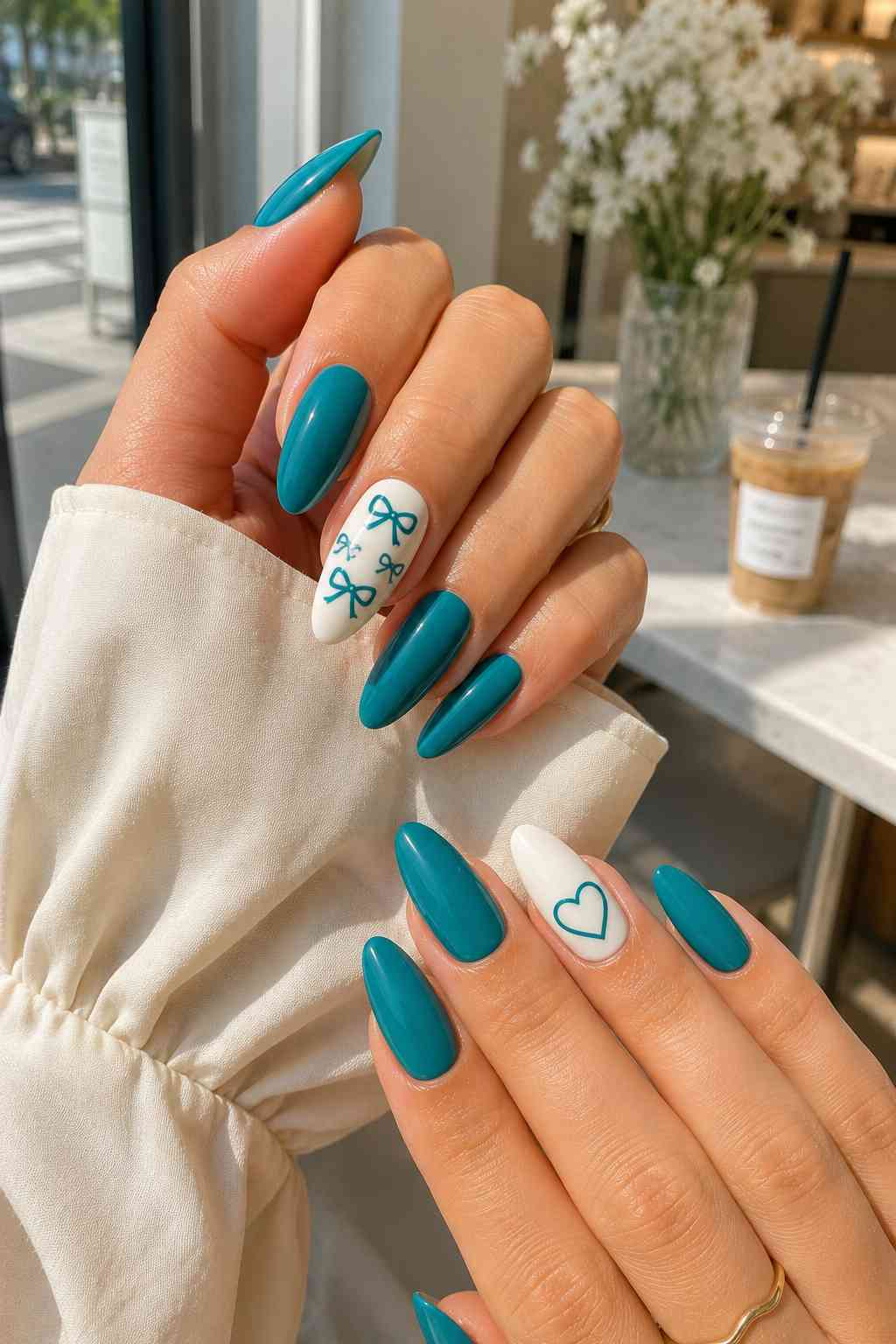 Glossy teal almond nails with white accent nails featuring teal bows and a heart design