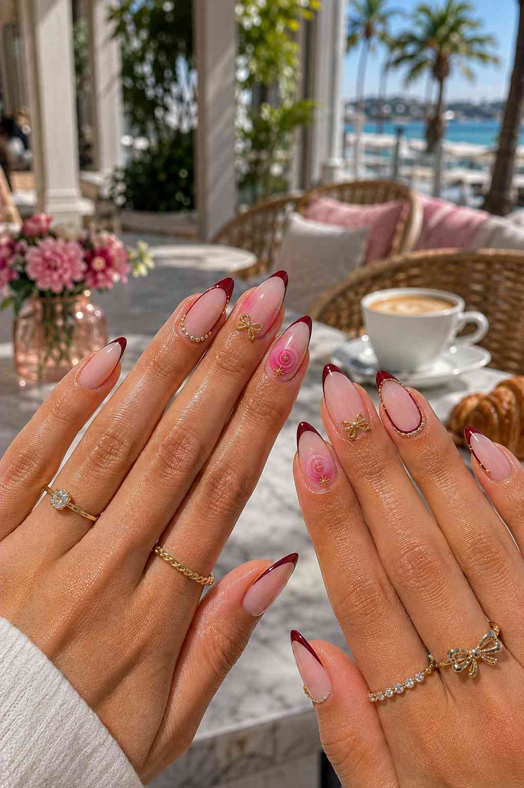 Deep wine French tip nails with gold bow charms, spiral art, and pearl and gold dot line detailing